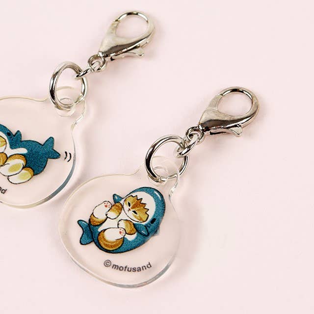 The Mofusand Mini Keychain Charm - 2 Piece Set by Mofusand features clear acrylic charms with a cat in a shark costume holding two smaller cats, labeled © mofusand and finished with silver clasps.