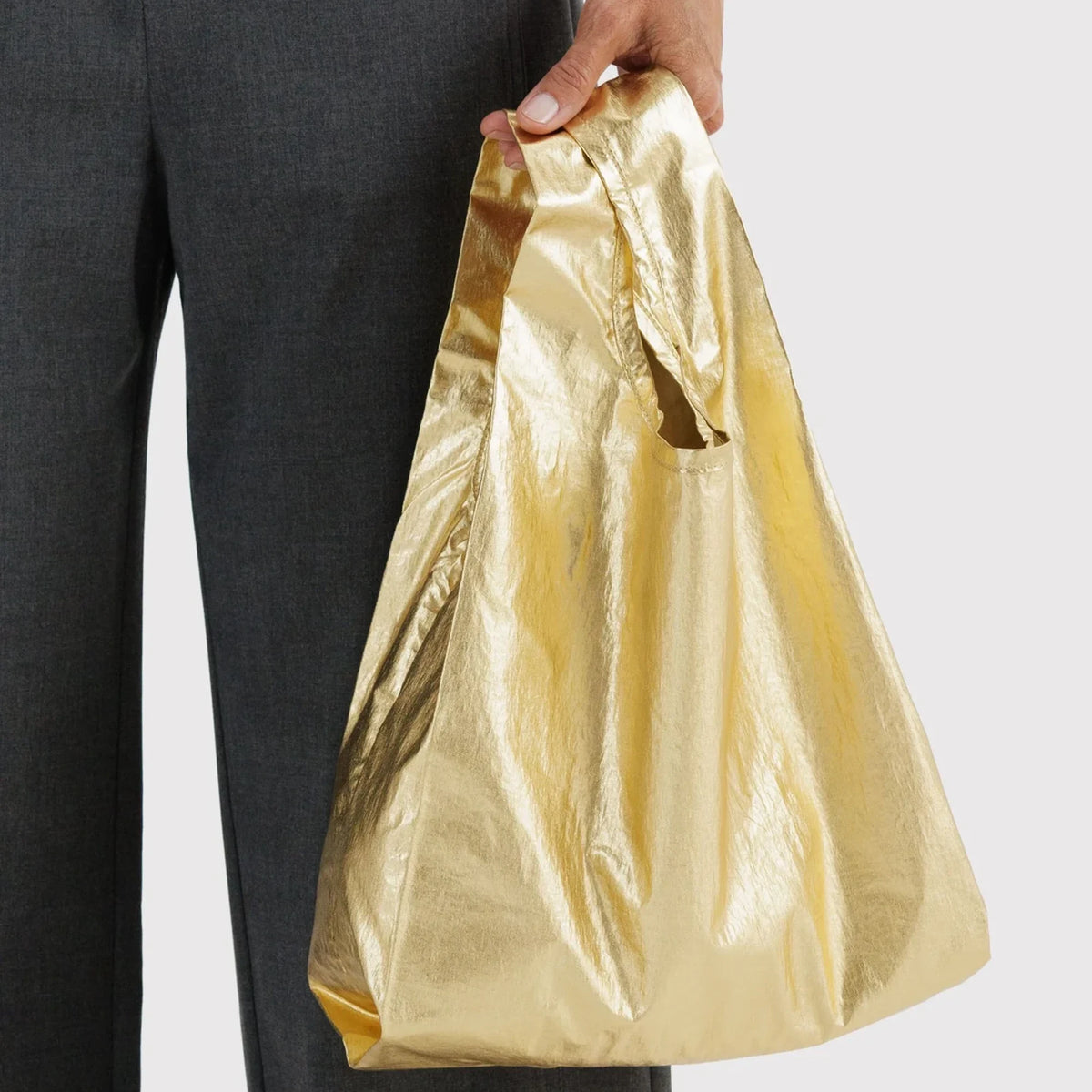 Gold metallic tote bag held by a person, roomy open shape