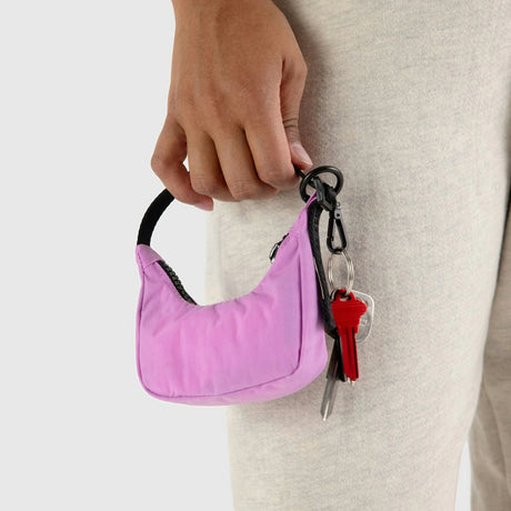 A person holds a small pink handbag, adorned with a Baggu Crescent Bag Charm in Cornflower, and a keyring with keys.