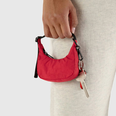 A person holding a Baggu Crescent Bag Charm in Cornflower blue with black straps and attached keys, wearing light-colored pants.