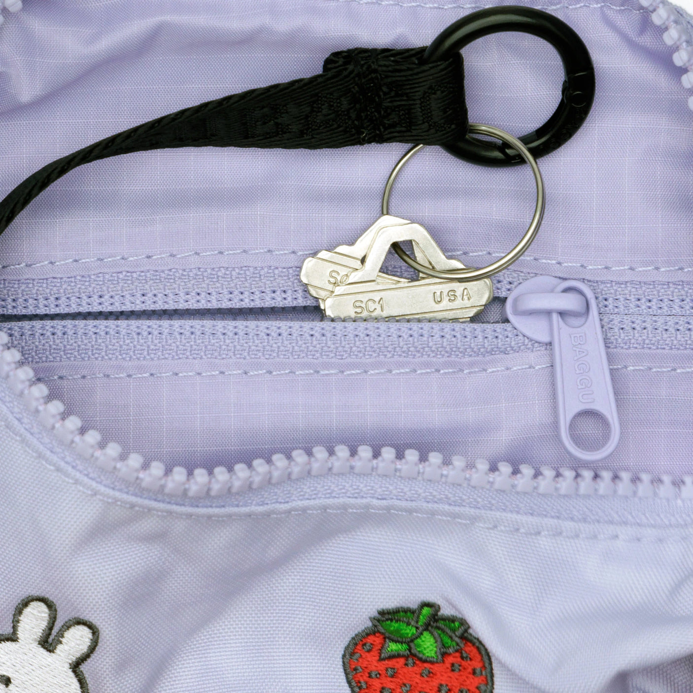 Close-up of two keys on a keyring inside the Baggu Miffy x Baggu Small Nylon Crescent bag in light purple, featuring embroidered patches such as a strawberry and Miffy.