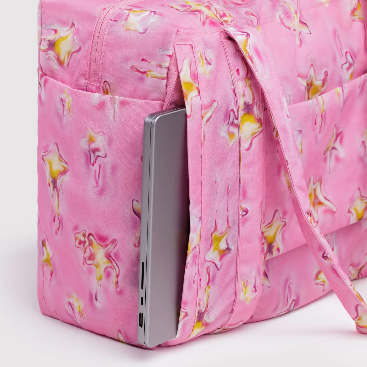 Pink star-print carry-on bag with front zip pocket holding smartphone