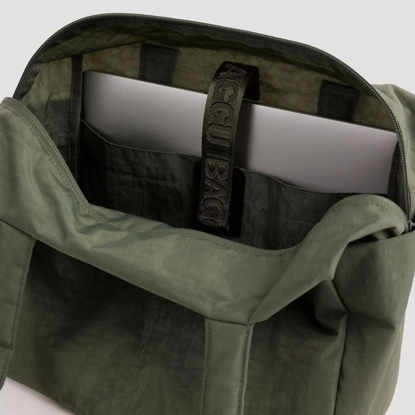 Olive green bag interior with zip pocket and label webbing strap