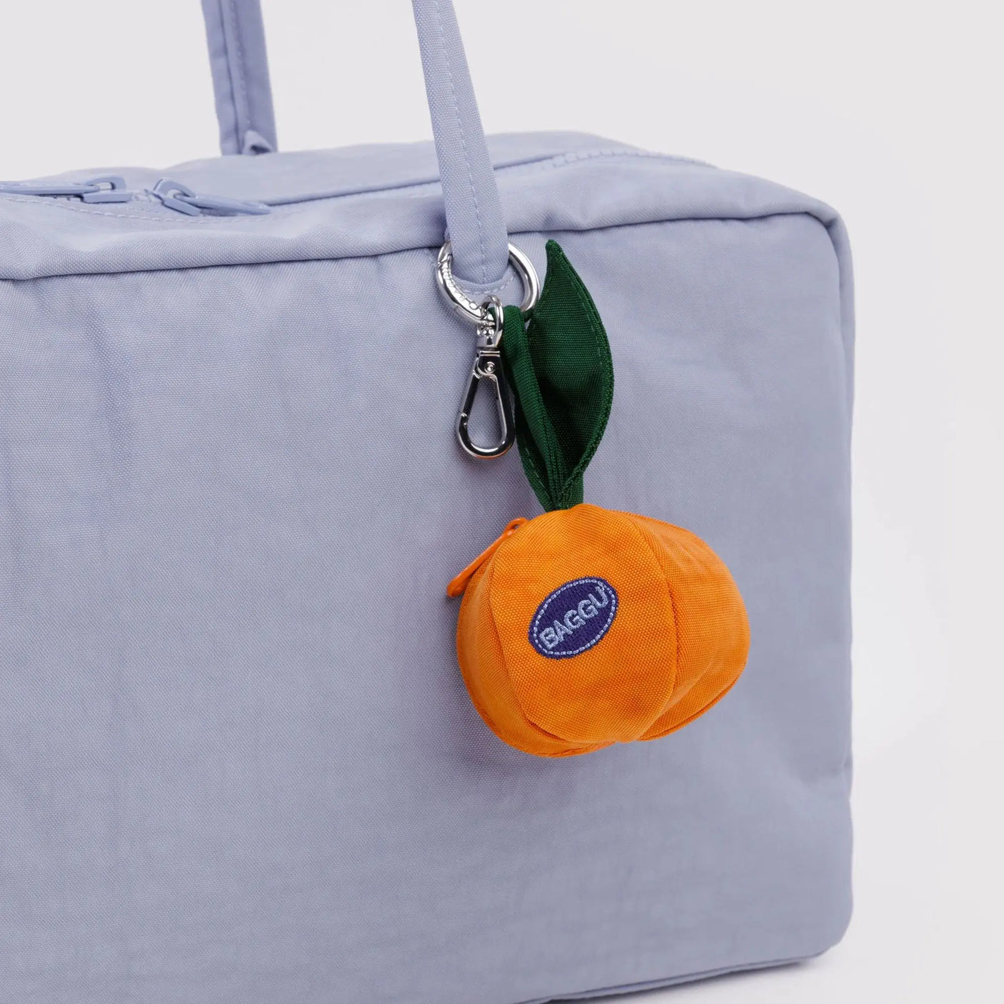 Orange Baggu bag charm with green strap and logo patch, attached by metal clip