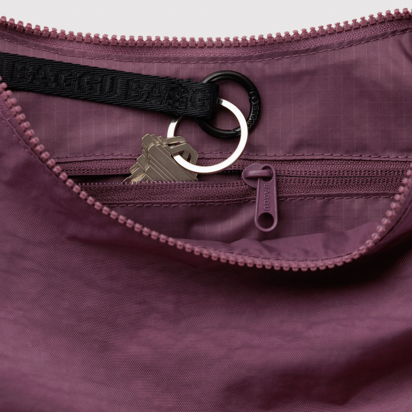 Wild plum nylon crescent bag interior with zipper, key ring, and dangling zip pull tab