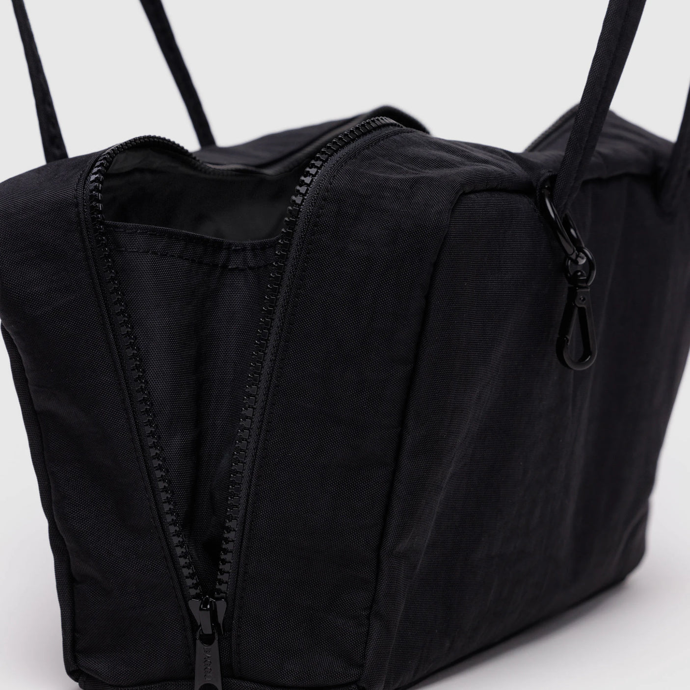 Close-up of the Baggu Nylon Bowler Bag - Black by Baggu, rectangular with a partially open zipper showing the interior and a strap clip. Made from recycled nylon for style and sustainability.