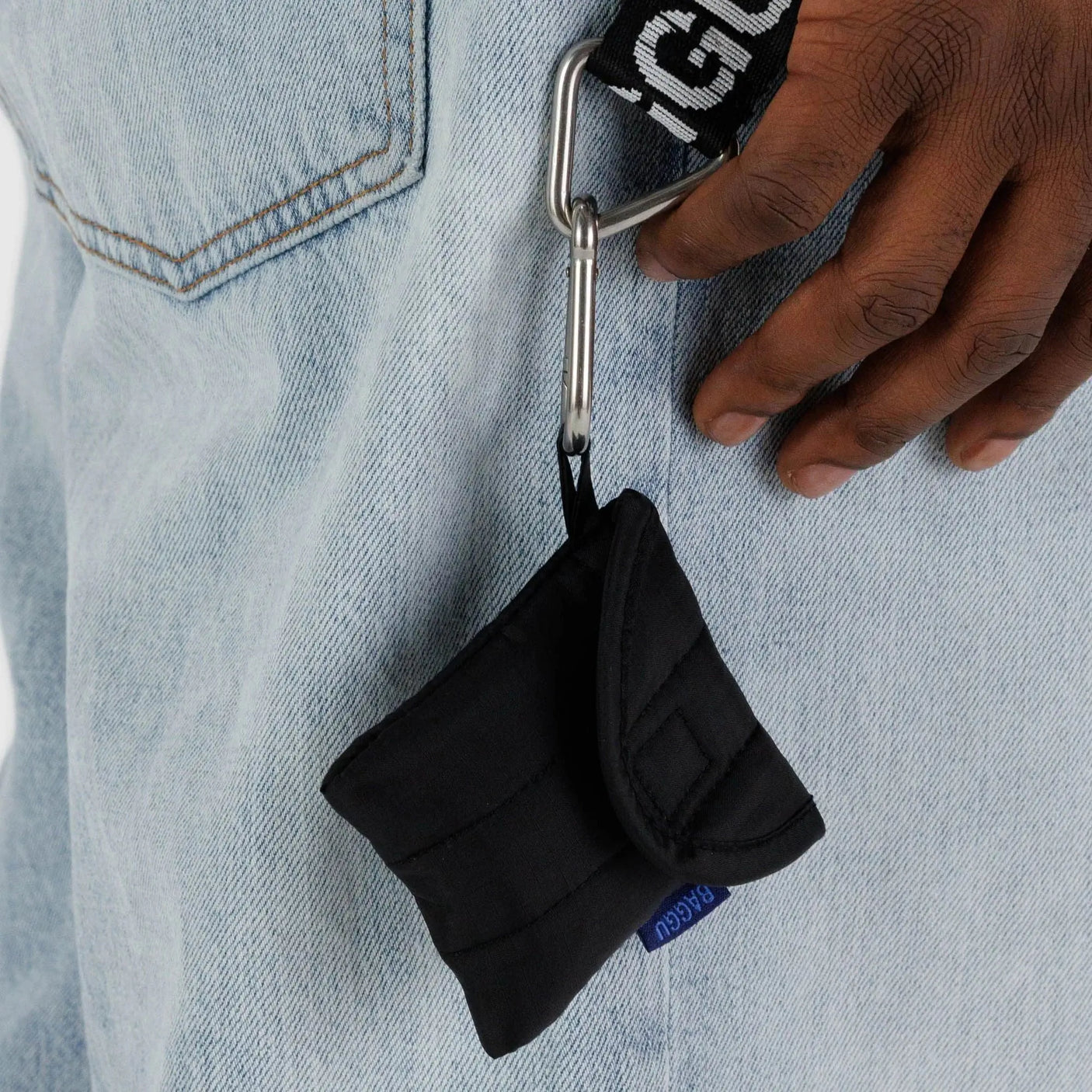 Black earbuds case with loop strap and metal clip, shown attached to denim