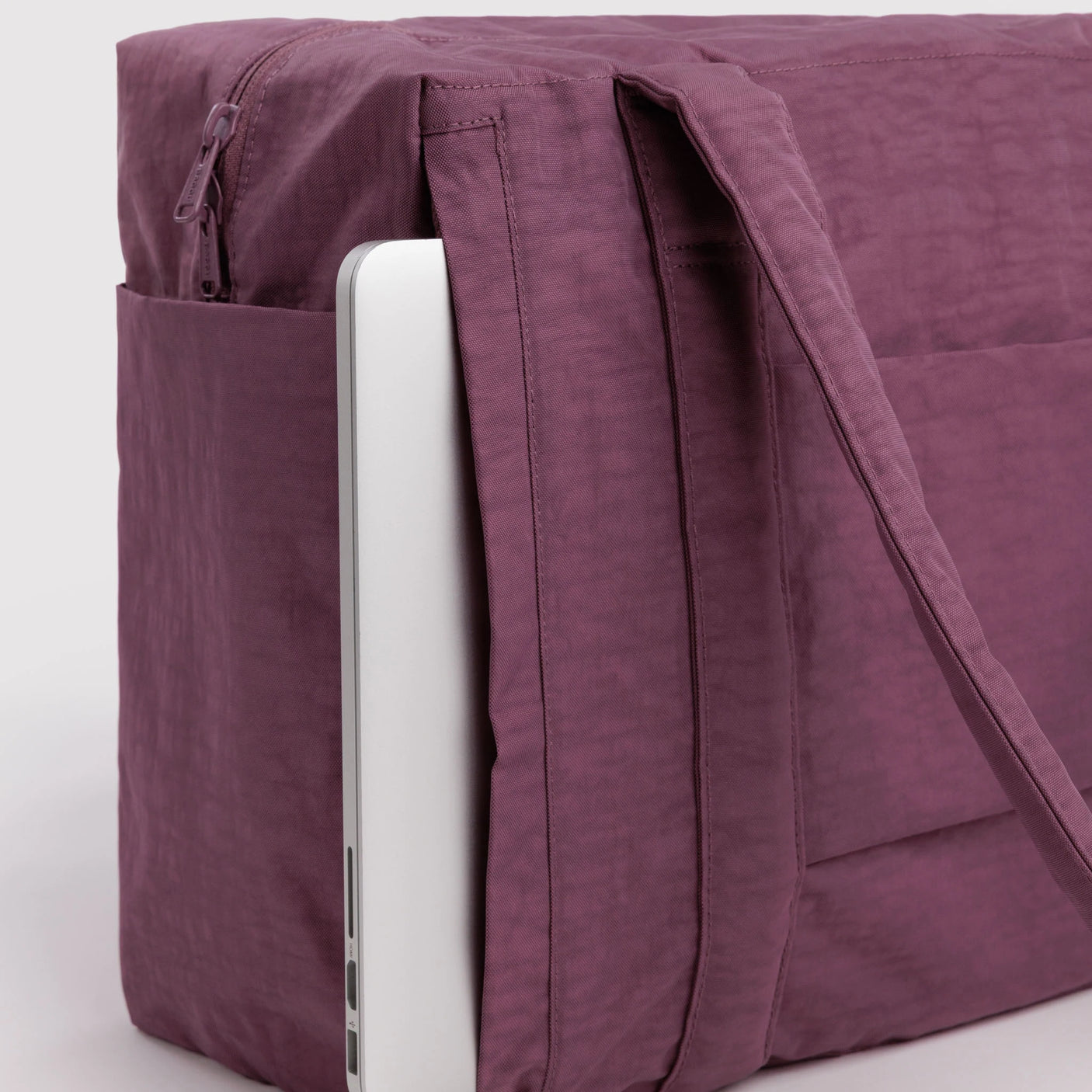 Plum carry-on tote bag close-up with side zipper, inner sleeve, and long strap
