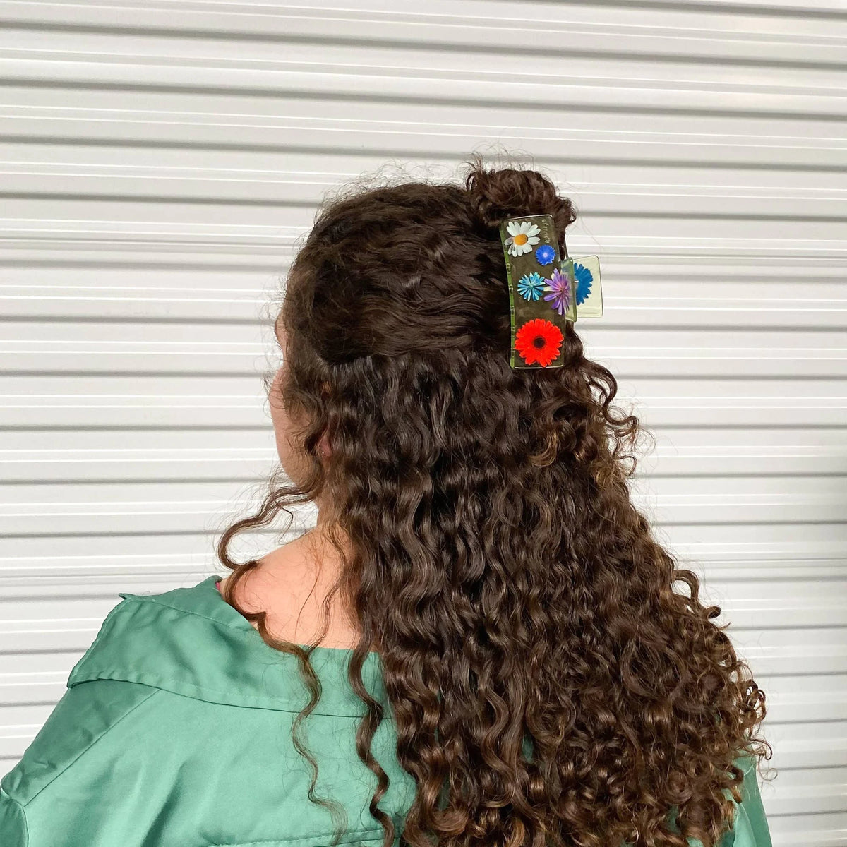 Flower claw clip on long dark curly hair with small colorful flower accents