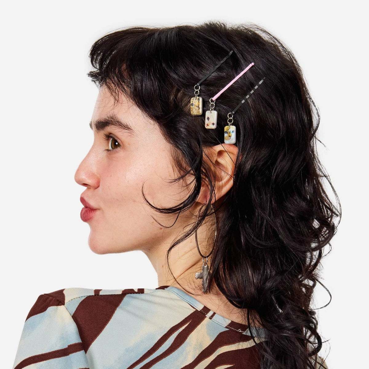 Cat charm bobby pins clipped in dark hair, with pink and gold accessory details