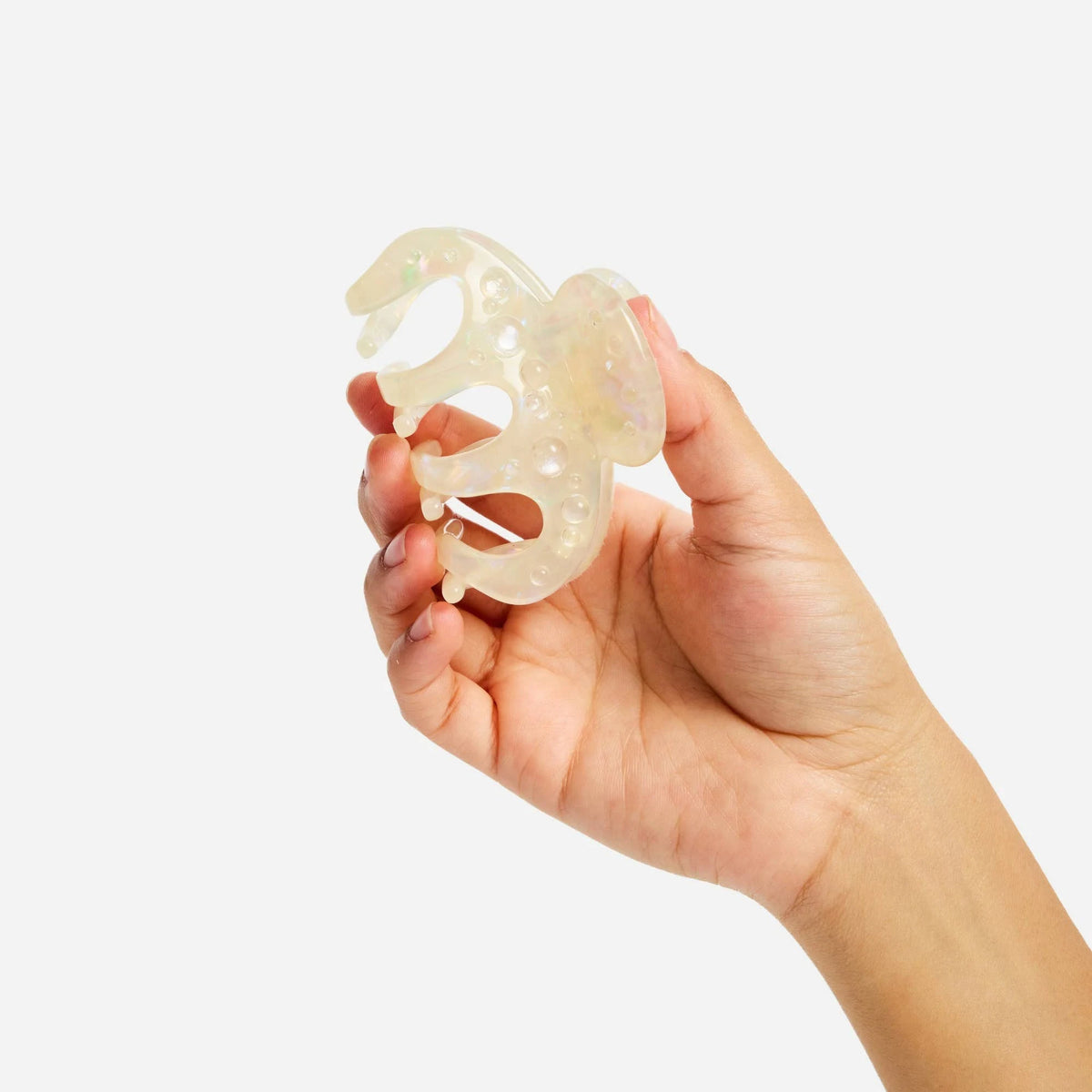 Small octopus claw hair clip close-up, translucent pearl-shimmer cream.