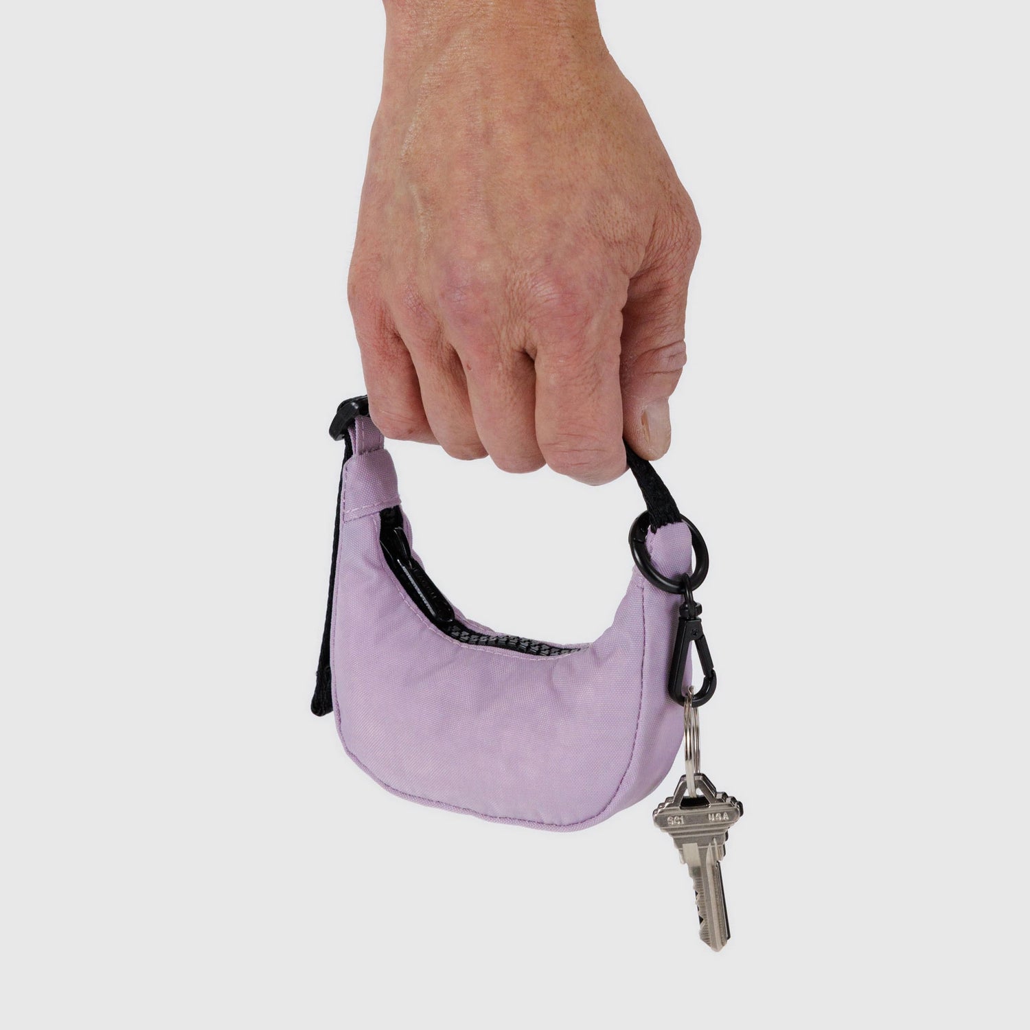 Hand holding a dusty pink Baggu Crescent Bag Charm with attached key on a metal clip against a white background