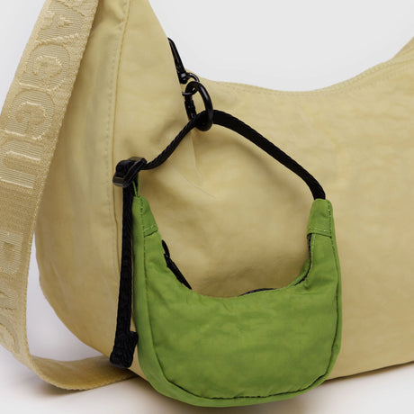 Green Baggu Crescent Bag Charm attached to beige shoulder bag with black strap and clip detail