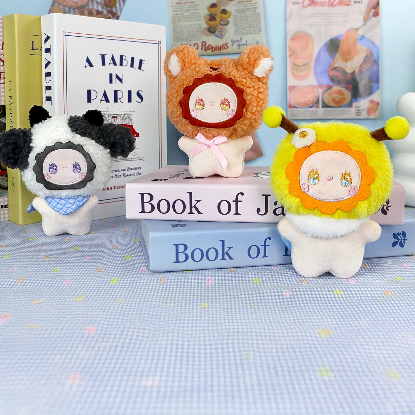 Three plush dolls from the Lucky Emma Emma Fuzzy Family Bag Charm - Blind Box are displayed on stacked books, with more books upright in the backgroundβperfect as a surprise charm or adorable accessory.