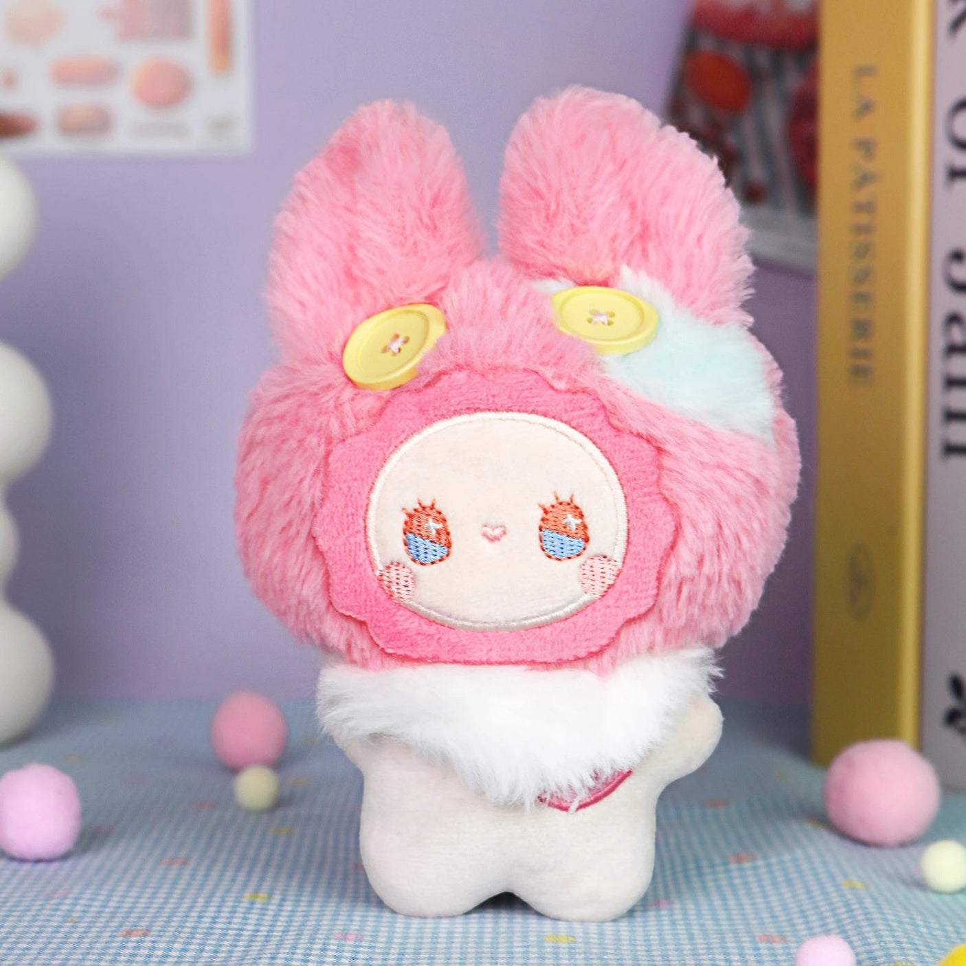 The Emma Fuzzy Family Keychain Blind Box by Lucky Emma features a plush toy with pink fur, yellow button eyes, and a white bodyβperfect as a cute keychain or bag charm for any collection. Pastel decorative background adds extra charm.