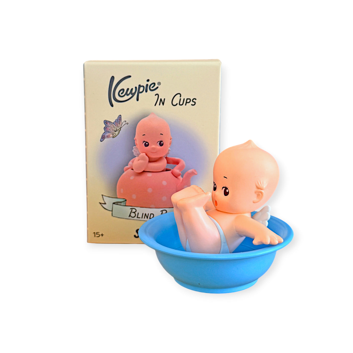 Small baby doll figurine with wings sitting in blue cup beside product box with butterfly illustration