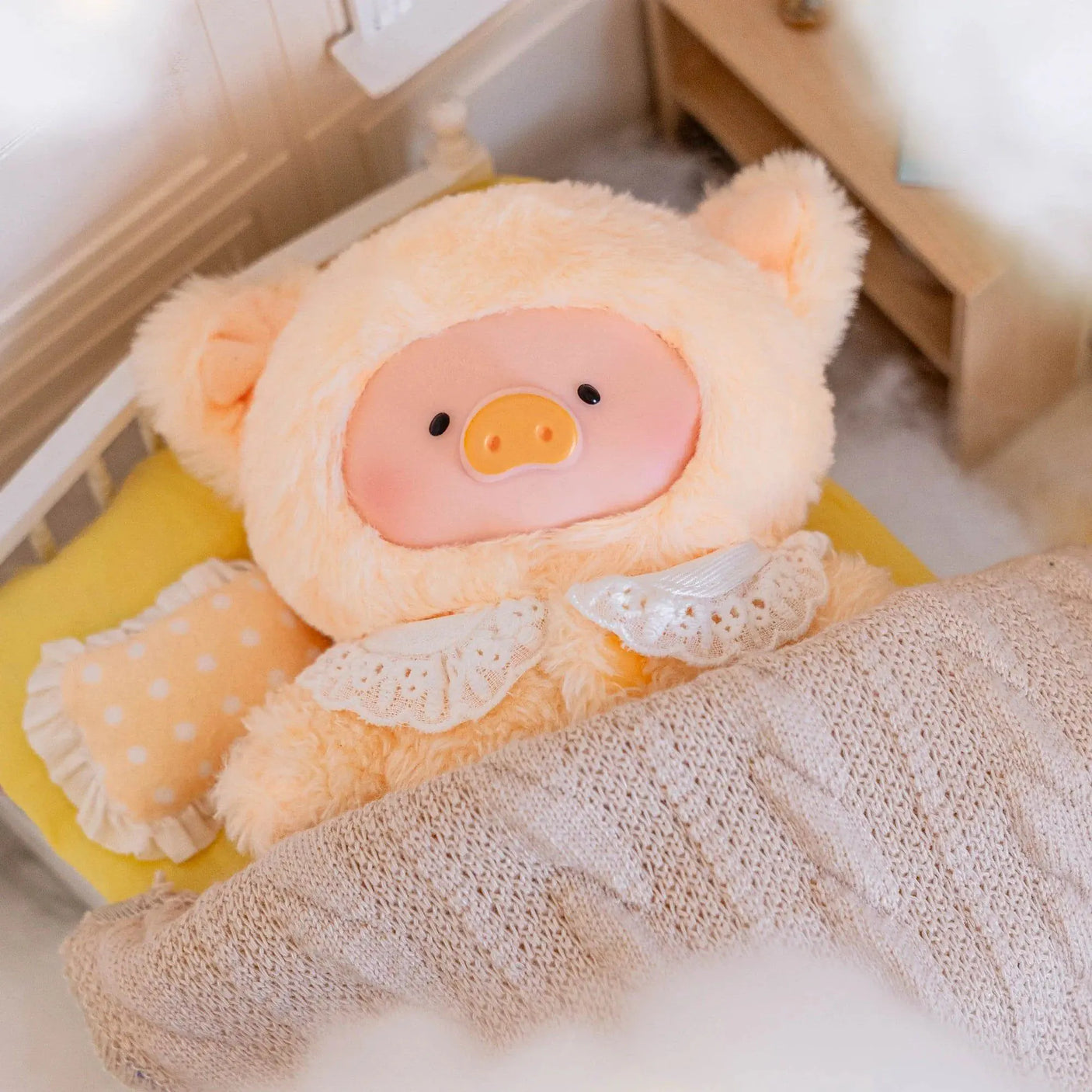 White plush piglet doll with orange snout, wearing white ruffled outfit on a knitted blanket