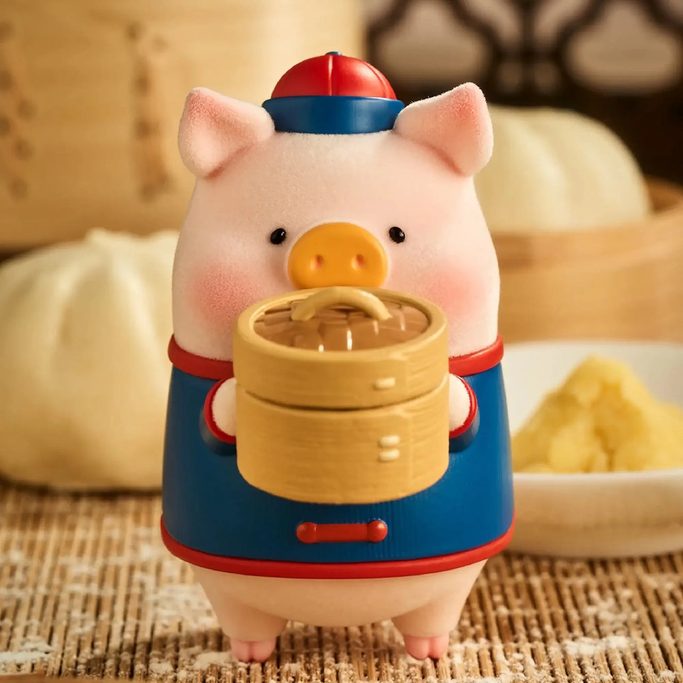 Pig chef figurine in a blue outfit holding a round wooden steamer lid pot