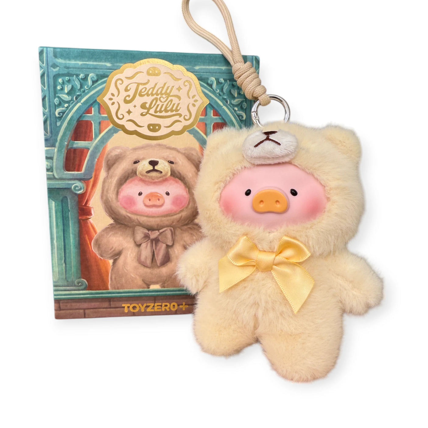 The LuLu The Piggy "Teddy LuLu the Piggy Plush Pal - Blind Box" keychain wears a yellow teddy bear onesie with a bow, displayed in front of matching LuLu The Piggy and TOYZERO+ packaging. A perfect collectible!