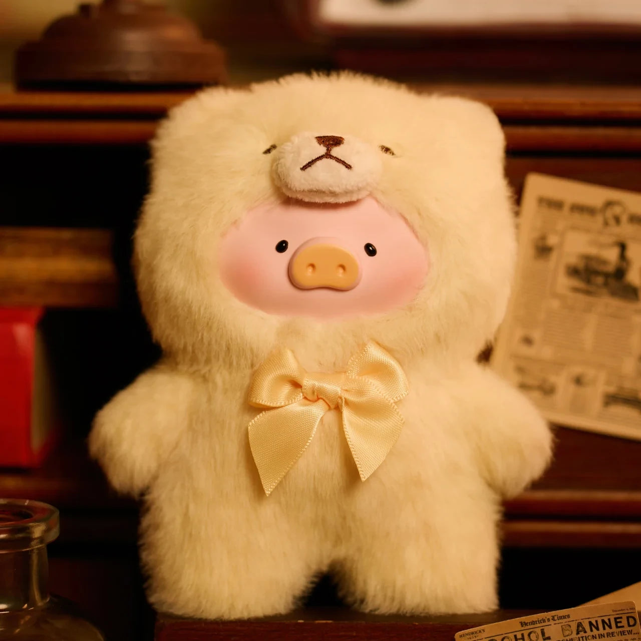 The LuLu The Piggy Teddy LuLu the Piggy Plush Pal - Blind Box features a piggy in a fluffy teddy bear onesie with a yellow bow, shown with vintage papers and wooden objects.