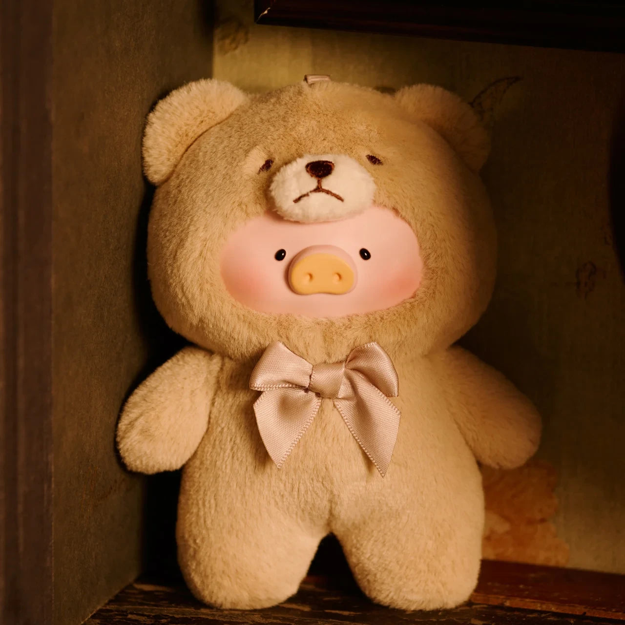 The LuLu The Piggy "Teddy LuLu the Piggy Plush Pal - Blind Box" features a pig face and a bear-shaped body with a light-colored bow, set against a dimly lit background.
