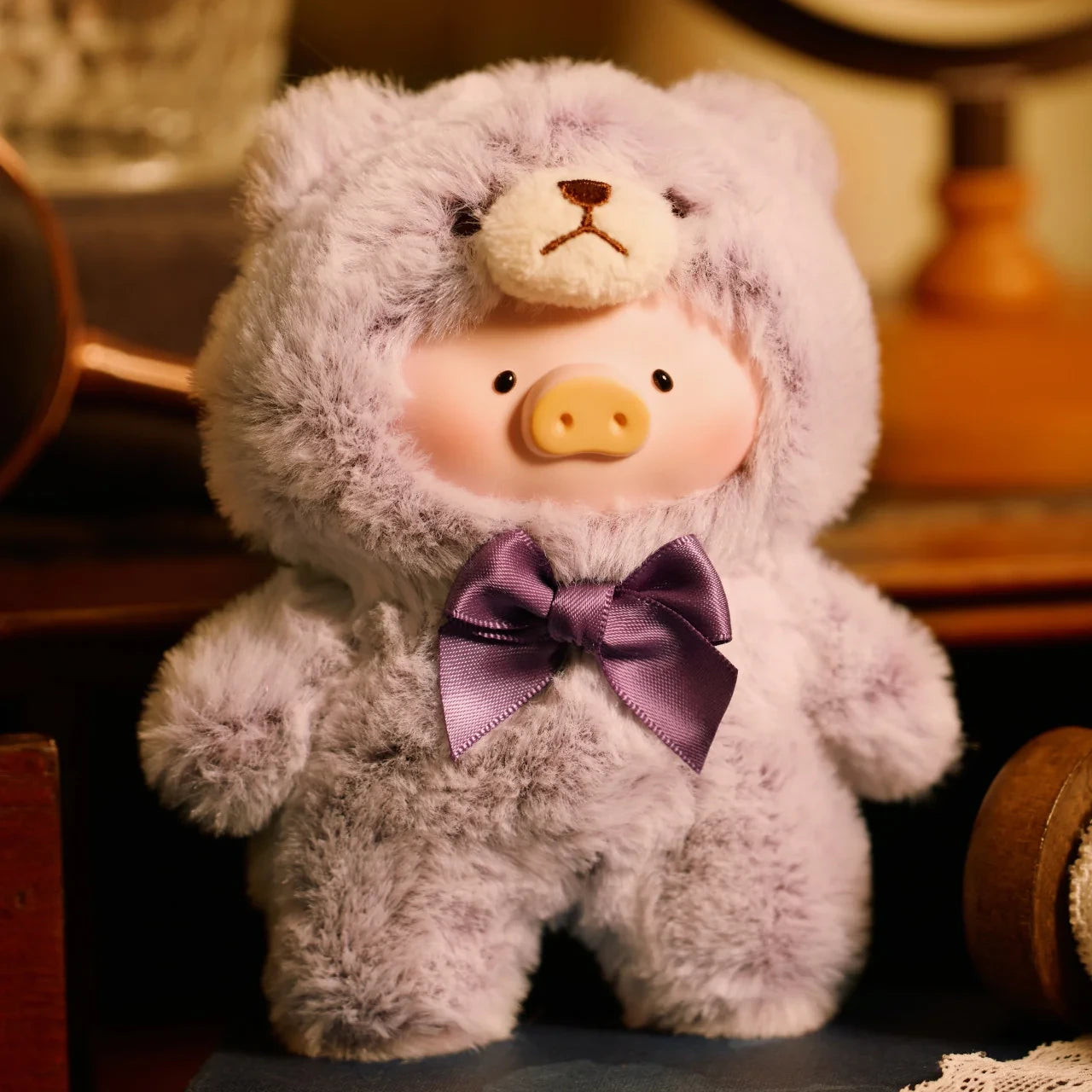 Teddy LuLu the Piggy Plush Pal by LuLu The Piggy wears a fuzzy purple teddy bear onesie with a matching bow, sitting cutely indoors—an irresistibly adorable Blind Box collectible.