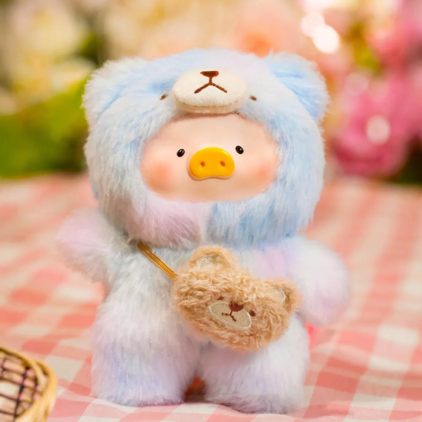 The Joyful Time Lulu The Piggy Plush Pal - Blind Box by LuLu The Piggy features a pig in a light blue bear costume, standing on a pink checkered surface with a bear-shaped bag and floral background.