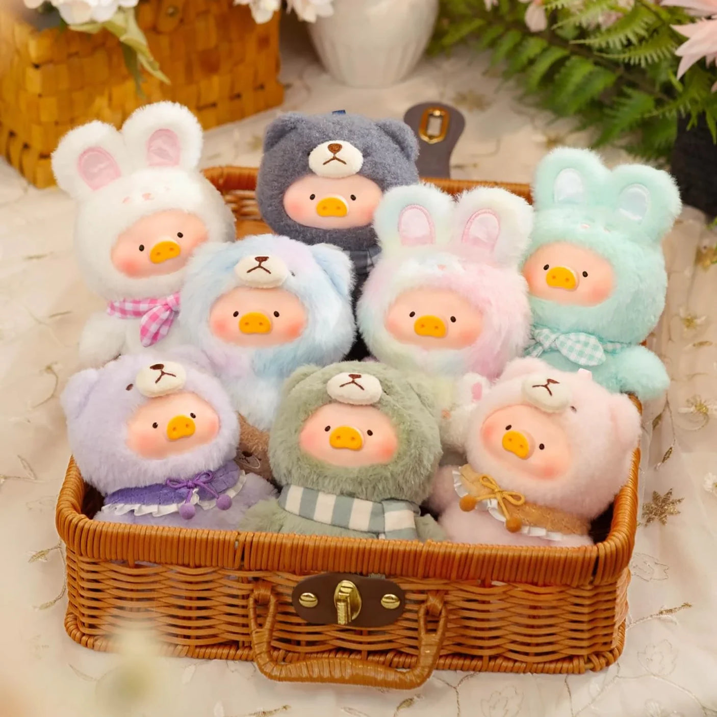 A wicker basket holds nine Joyful Time Lulu The Piggy Plush Pal - Blind Box toys by LuLu The Piggy, each a cute round plush with colorful fur, pig noses, and various hoods—perfect for keychain plush collectors.