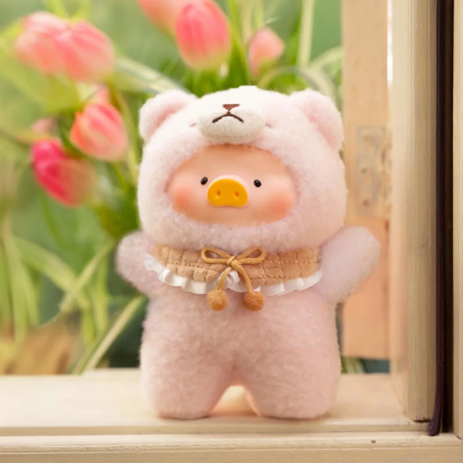 A Joyful Time Lulu The Piggy Plush Pal - Blind Box from LuLu The Piggy, dressed in a fuzzy bear costume, stands by a window with pink tulips in the background.
