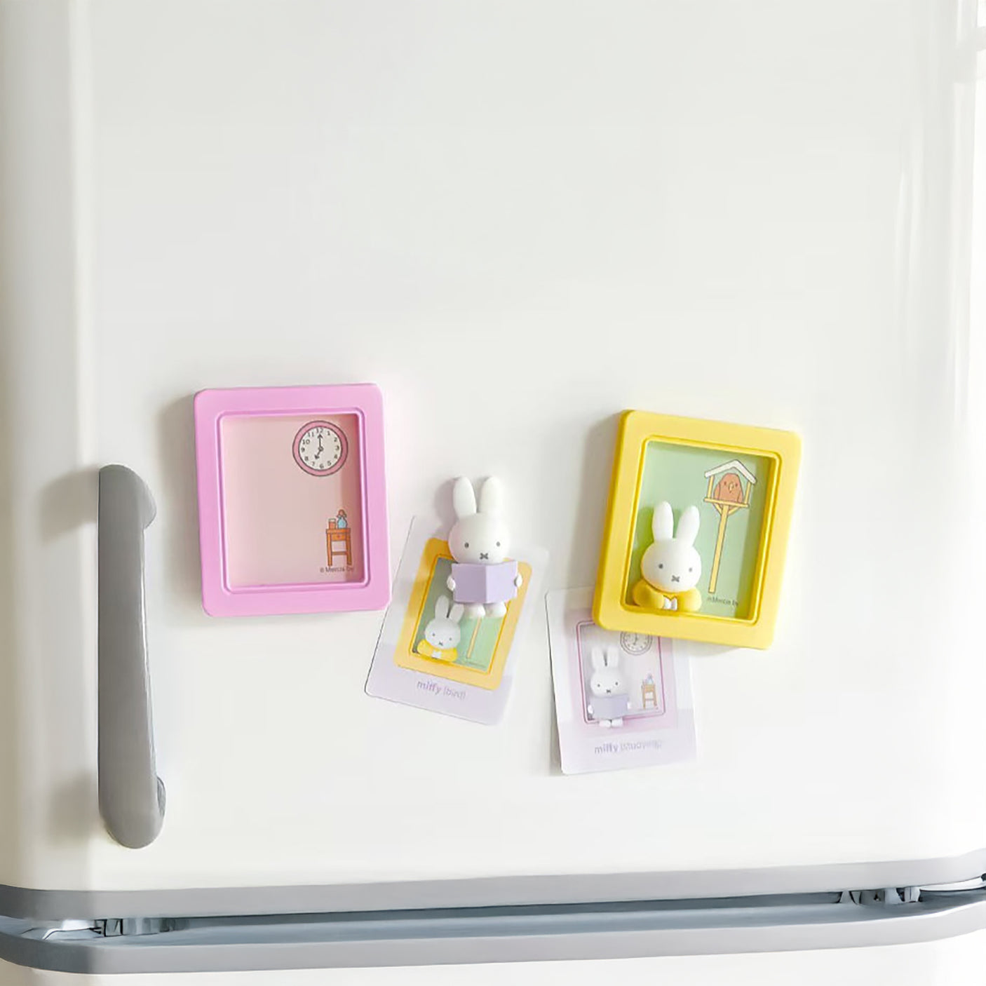 Two Miffy magnetic photo frames in pastel pink and yellow with small bunny figures on white fridge door