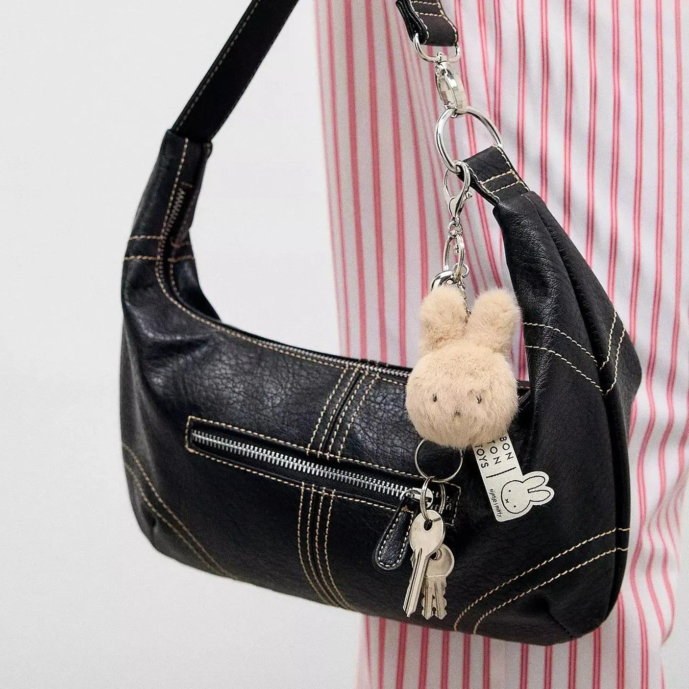 Beige plush rabbit keychain charm with metal ring attached to black bag strap.
