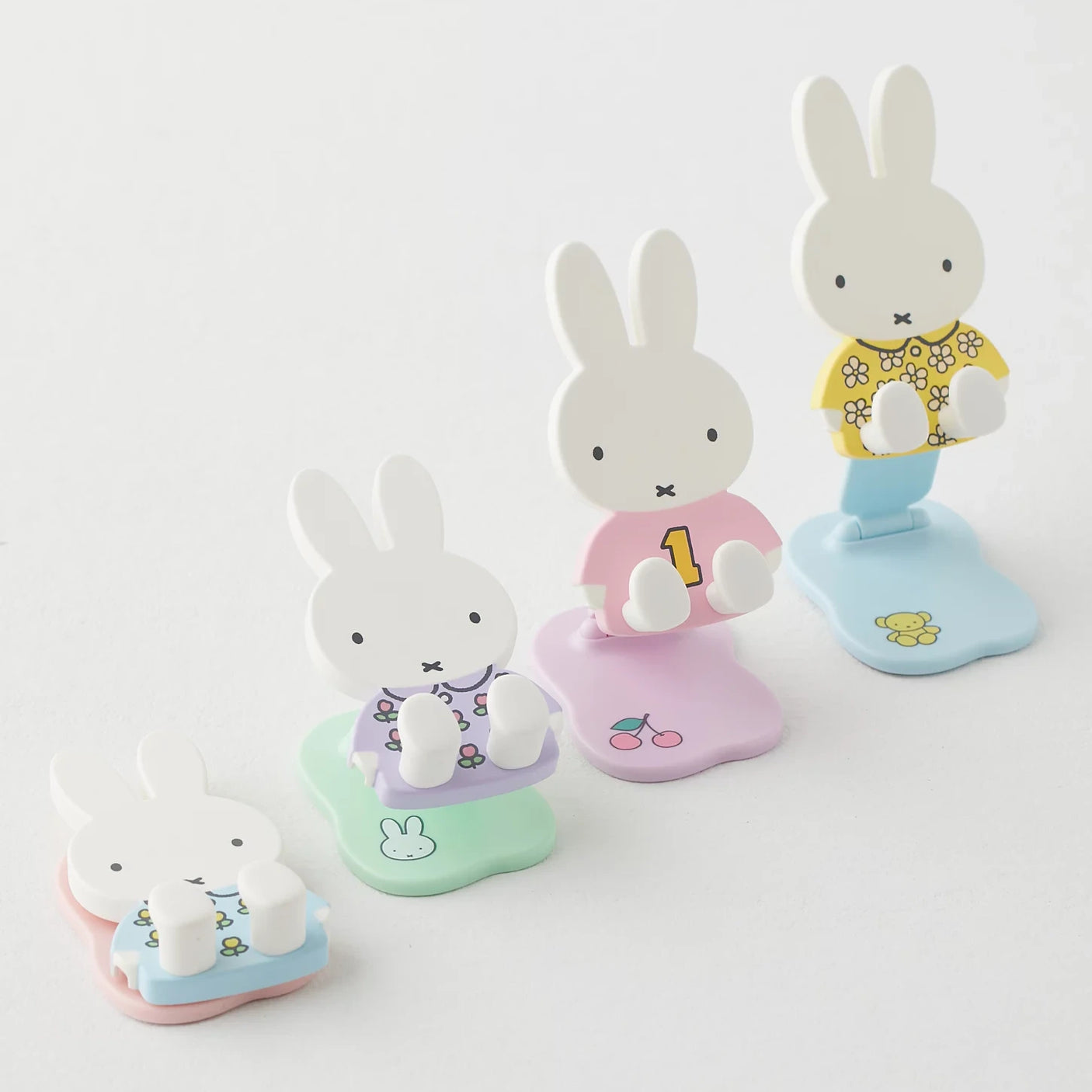 Four pastel Miffy phone and tablet stands folding open and flat, featuring various colorful outfits and base designs on white background
