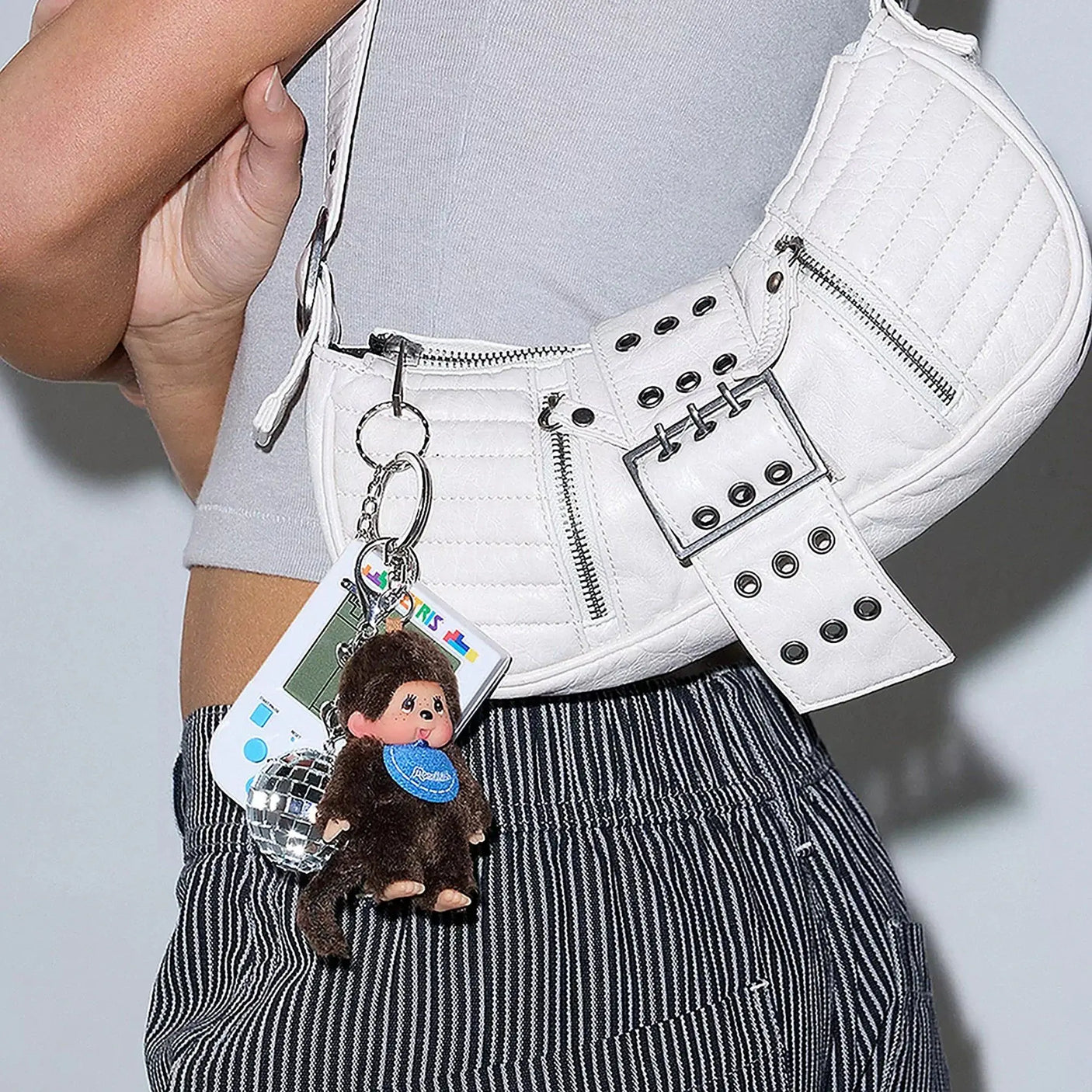 Brown plush Monchhichi keychain with blue scarf attached to a white bag
