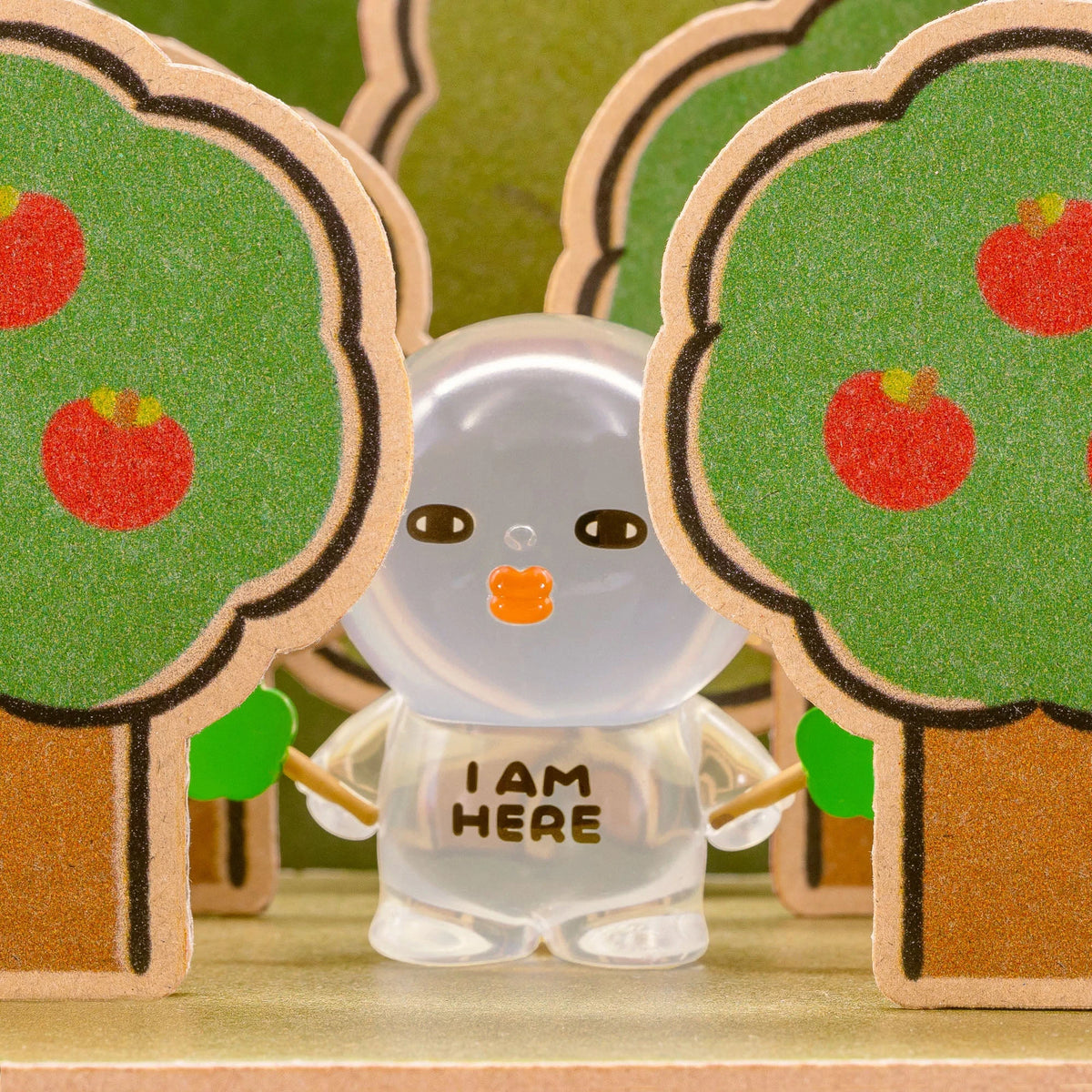 Clear-sleeve blind-box figurine standing between green hedges with orange emblem.