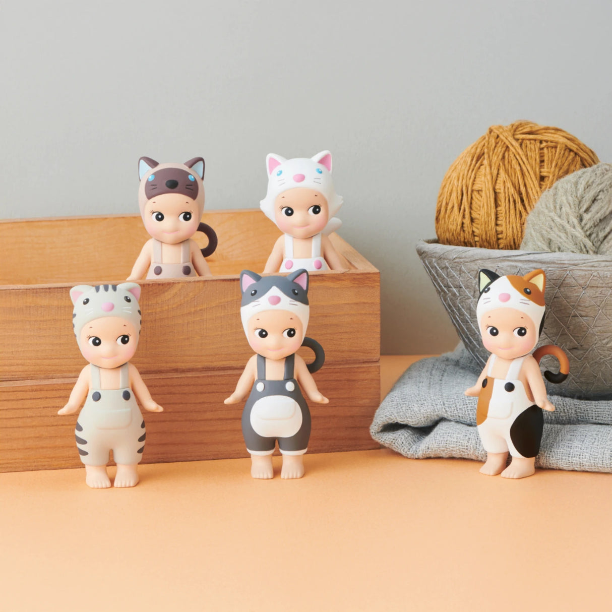 Five figures from the Sonny Angel Cat Life Series, a limited edition collection by Sonny Angel, are displayed on a table adorned with yarn balls and a wooden box, capturing their unique charm.