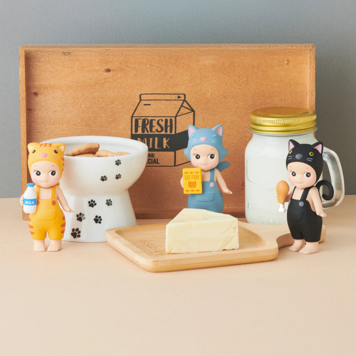 Three figures from the Sonny Angel Cat Life Series – Blind Box are set near a wooden tray with butter, a bone-shaped bowl with cookies, and a jar labeled "Fresh Milk." This Limited Edition from Sonny Angel adds charm to any collection.
