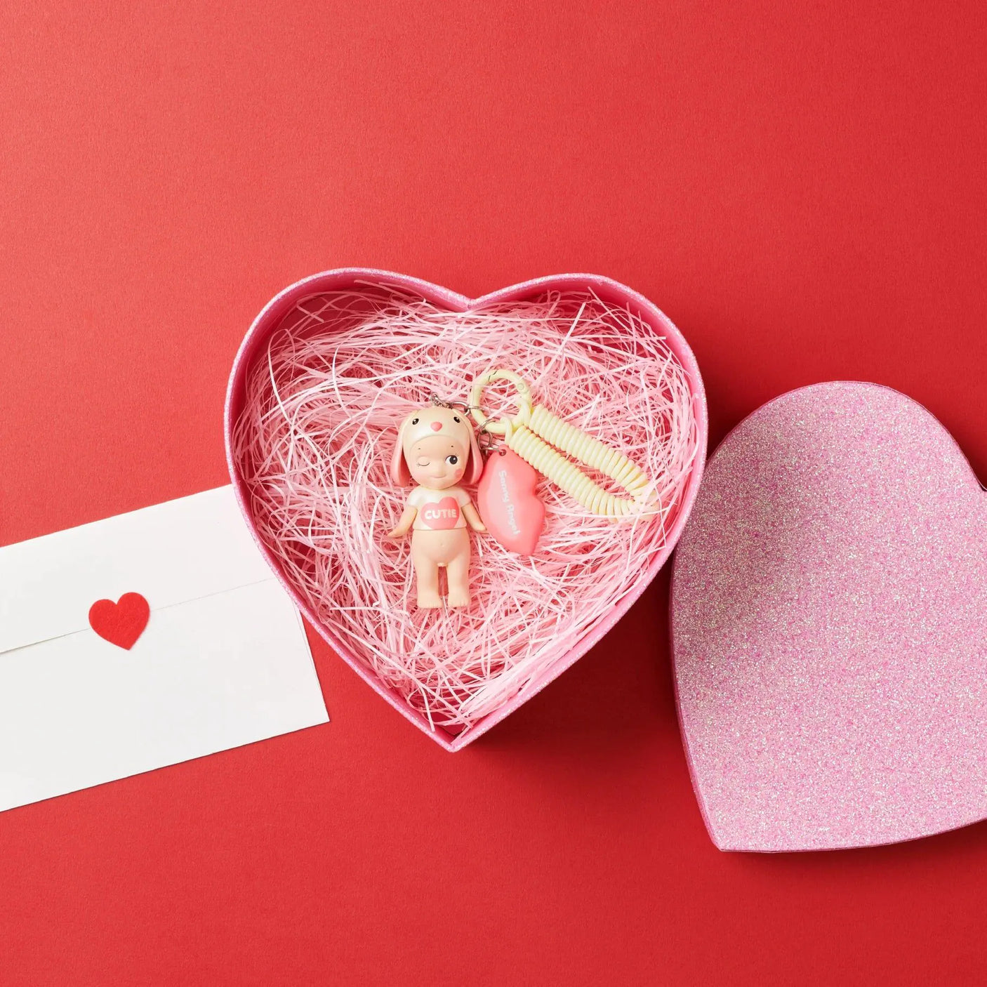 The Sonny Angel Kiss Kiss Series - Blind Box features a heart-shaped box with pink straw holding a small doll and charms. Bes