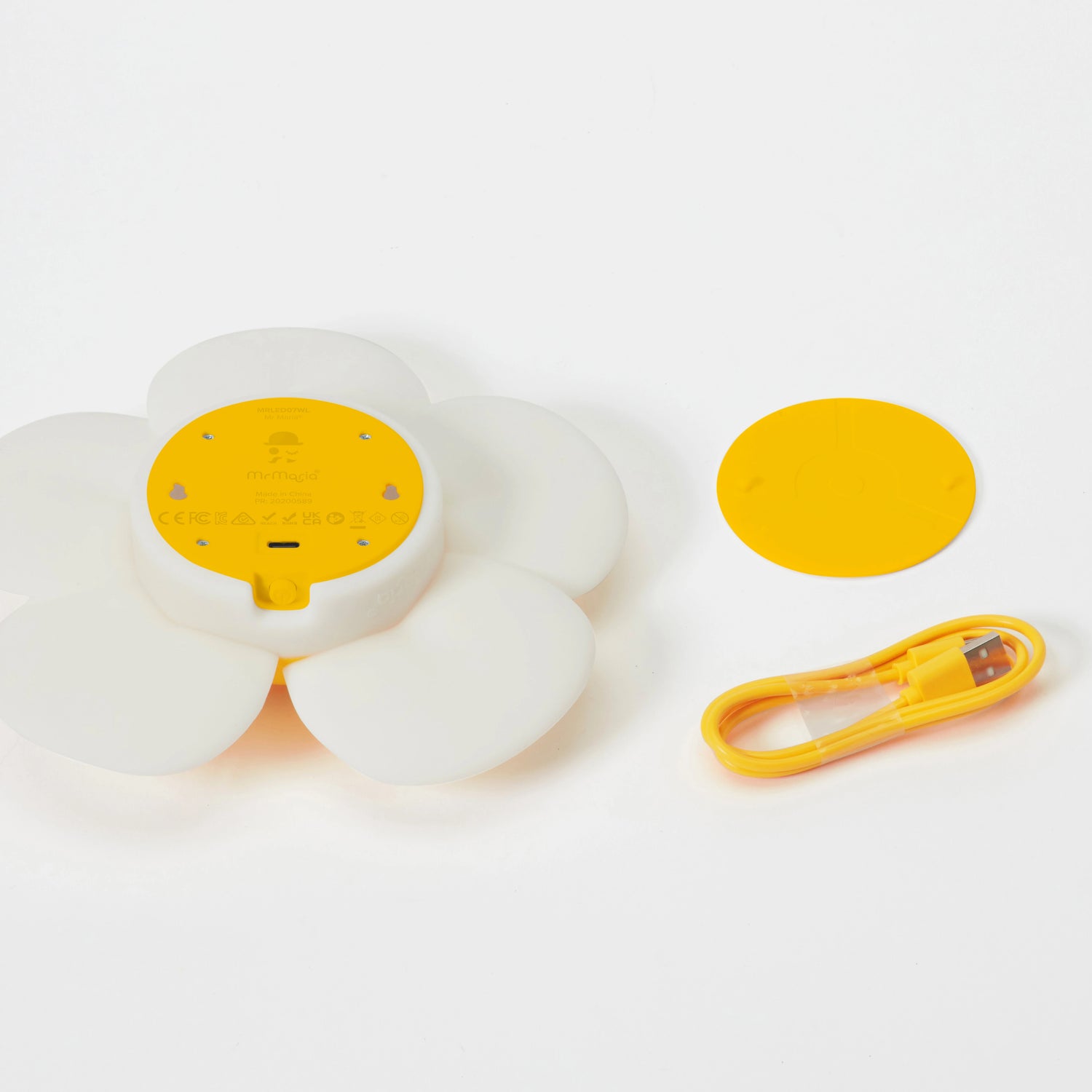 The Mr Maria Smiley Daisy - Day & Night Light, a retro white and yellow flower-shaped device, is shown with its matching yellow cover and USB charging cable, all neatly arranged on a white background.