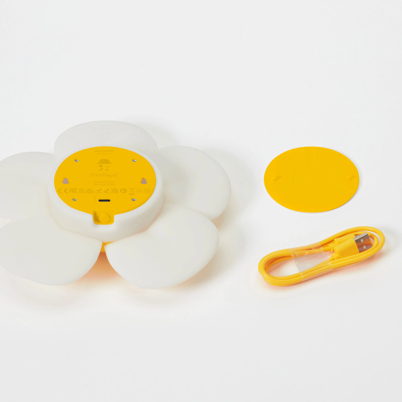 The Mr Maria Smiley Daisy - Day & Night Light, a retro white and yellow flower-shaped device, is shown with its matching yellow cover and USB charging cable, all neatly arranged on a white background.
