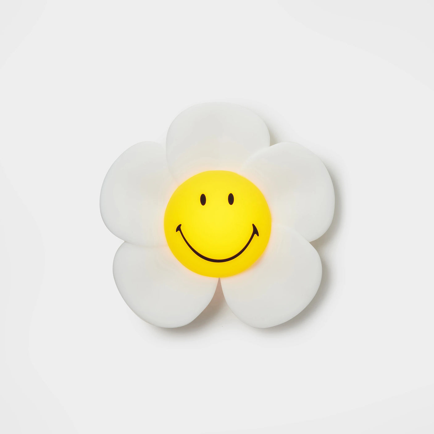 The Mr Maria Smiley Daisy - Day & Night Light is a decorative wall light shaped like a retro flower, with white petals, a yellow center, and a black smiley face, shown against a plain white background.