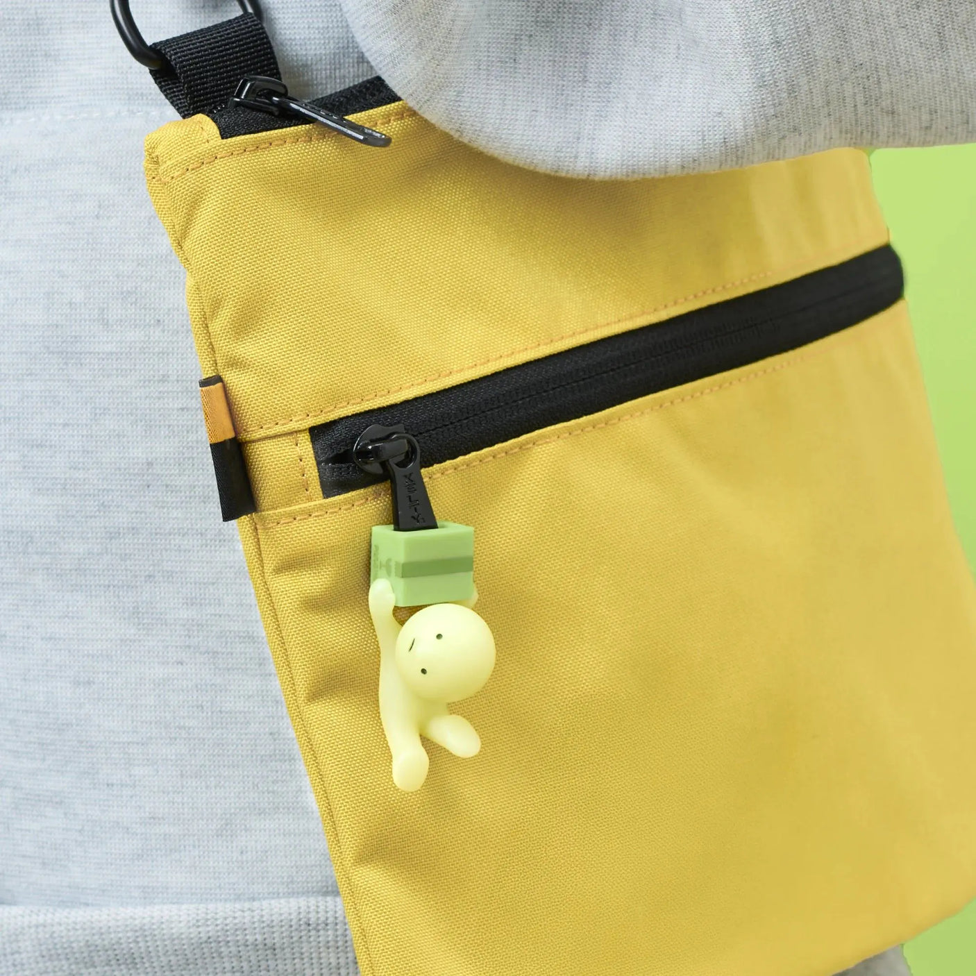 Smiski ZipperBite Falling Down figure charm hanging from yellow zipper pouch