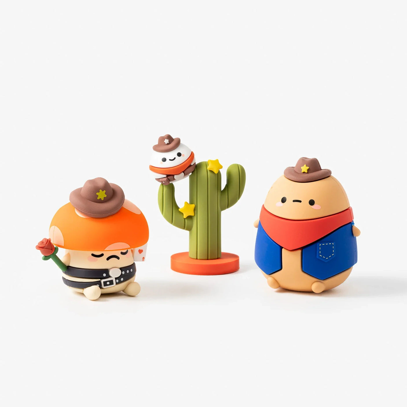 Three rounded toy figures dressed as cowboys with hats, a scarf, and a cactus decorated with stars on a white background