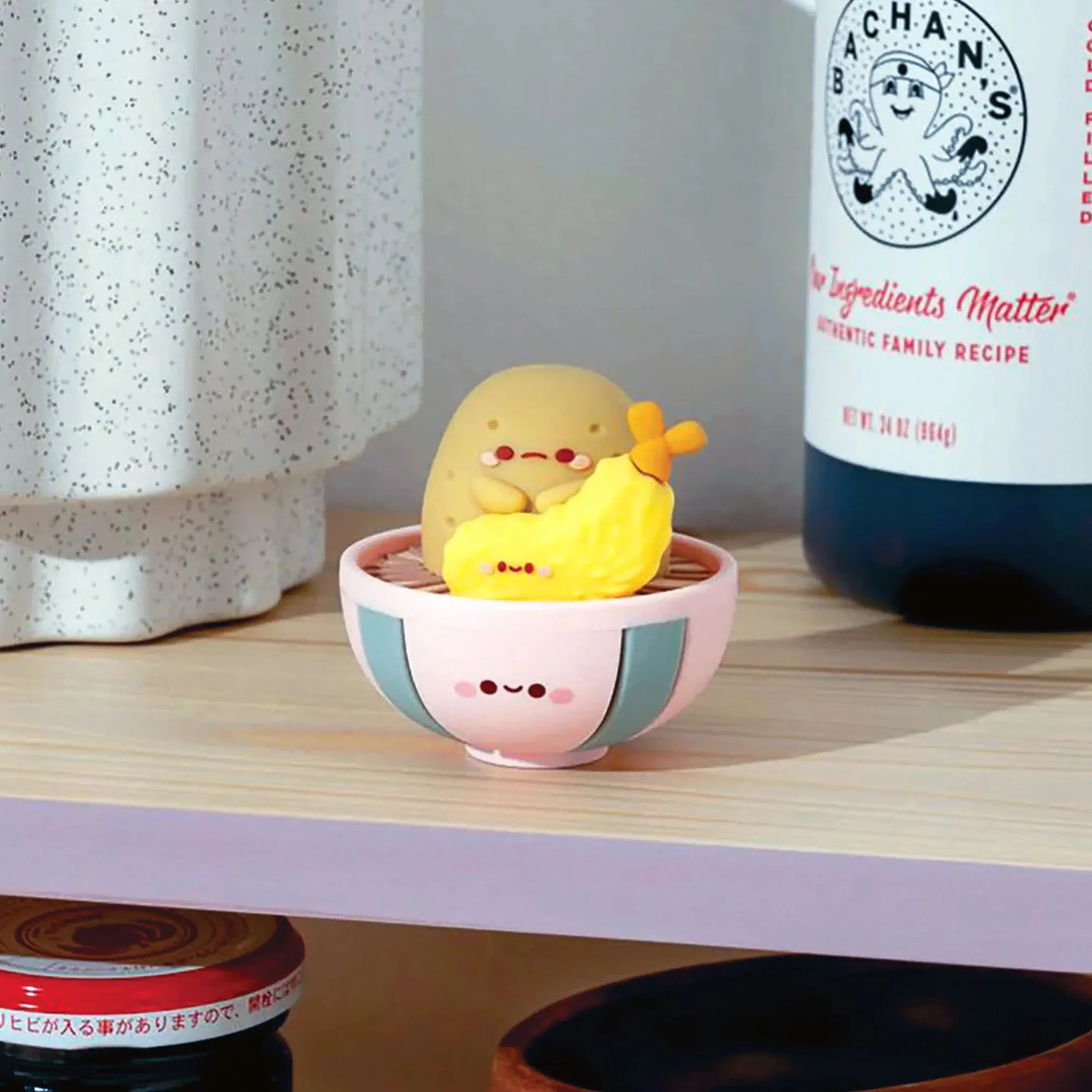 A charming Smoko Tayto Potato Ramen Blind Box figurine, known for its adorable face, rests in a pink bowl beside a smiling ba