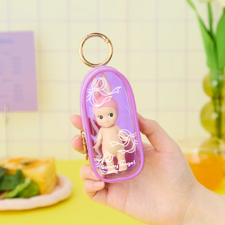 A hand holds the Sonny Angel My Bestie Case - Purple by Sonny Angel, a transparent mini figure carry case with a gold keyring that keeps your doll secure and stylish.