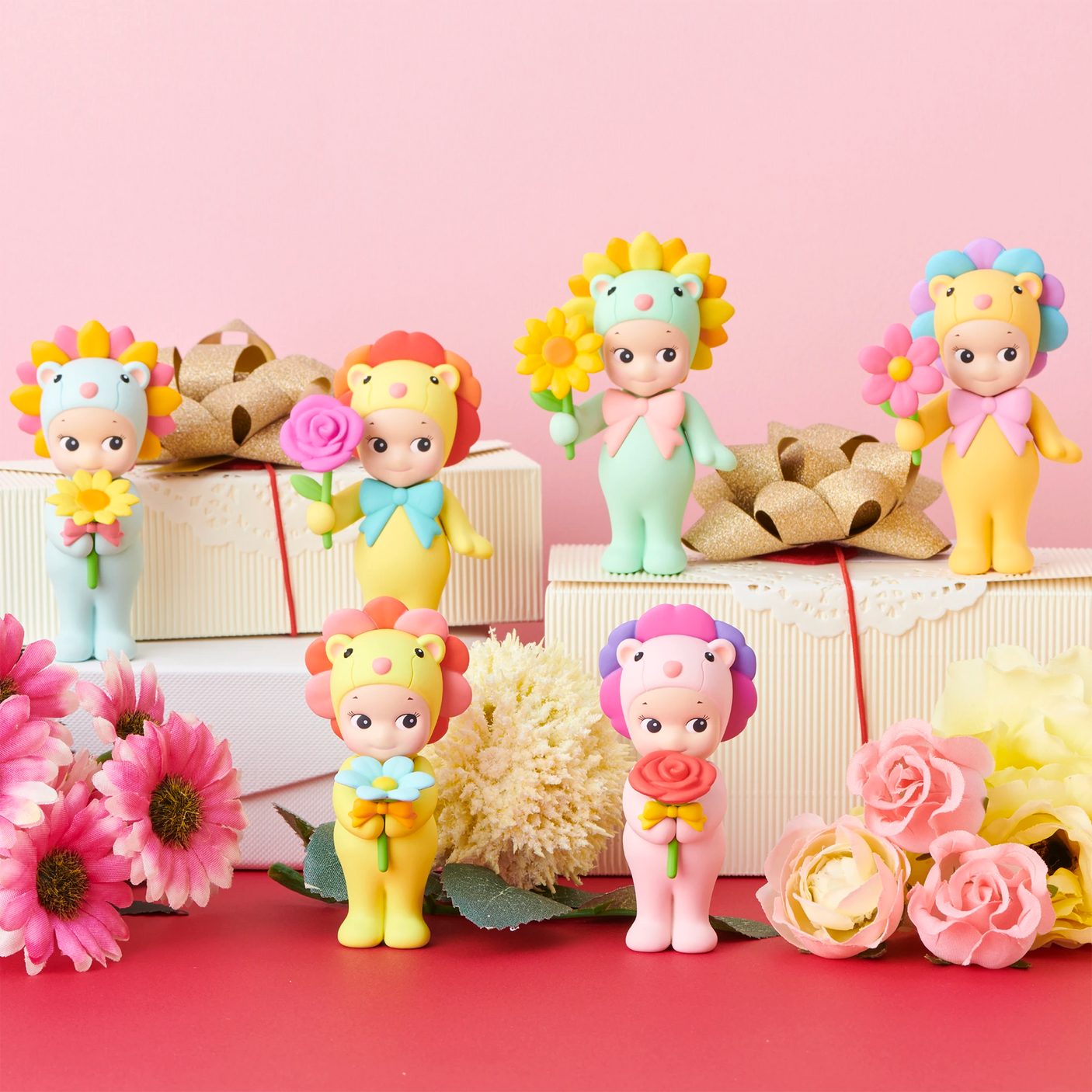 Six Sonny Angel Flower Gift Series figurines by Sonny Angel, each with a lion theme and holding flowers, are arranged on white gift boxes with artificial flowers on a pink background.