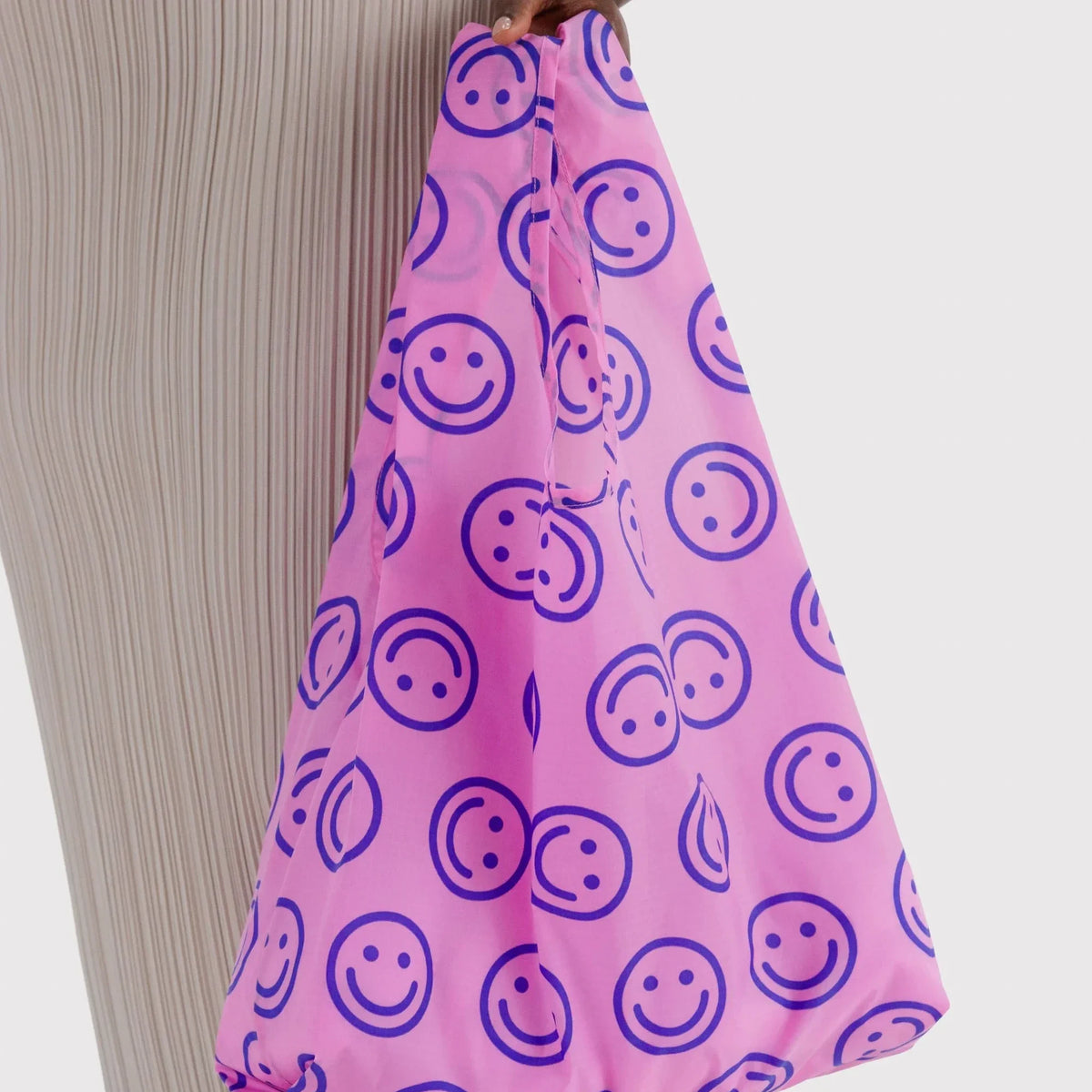 Pink tote bag with navy smiley face print, held by the strap