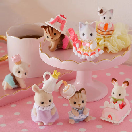 The Sylvanian Families Blind Bag - Baking Baby Party by Sylvanian Families features adorable animal figurines in pastel outfits with a pink cake stand, tea set, and mini desserts for a sweet celebration on a pink polka-dotted surface.