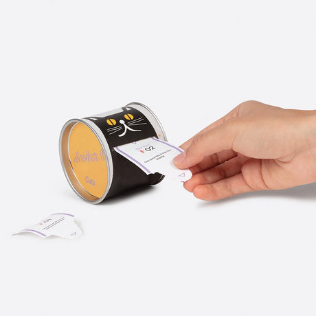 Hand pulling daily curious cat fact card from black cat-themed tin labeled Another Me Cats, gallery position 1