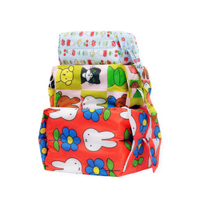 Three rectangular gifts, wrapped in colorful paper inspired by the Miffy x Baggu - Storage & Travel Set from Baggu, are stacked atop each other against a white background.