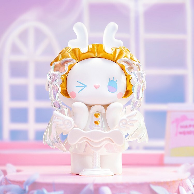 The Lucky EMMA - Secret Forest Wedding figurine by Lucky Emma showcases a whimsical design with bunny ears, a gold headpiece, translucent wings, and a winking face. Its collectible quality is enhanced by the soft pink and white background.